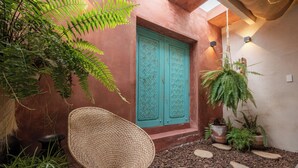 Un espacio al aire libre acogedor con una silla tejida, una puerta turquesa y plantas en macetas.