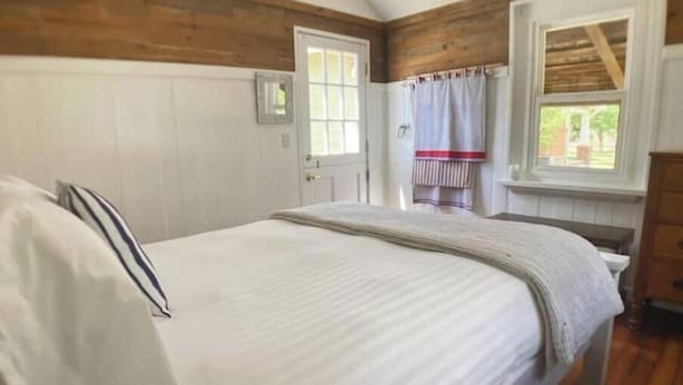 Ein Schlafzimmer mit einem großen Bett, Holzwandverkleidung, einem Fenster mit Vorhang und einer Tür.