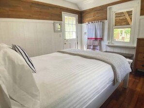 Un dormitorio con una cama grande, paneles de madera en las paredes, una ventana con cortina y una puerta.
