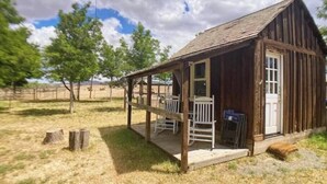 Eine rustikale Holzhütte mit Veranda und einer Tür, umgeben von einem eingezäunten Bereich und Bäumen.