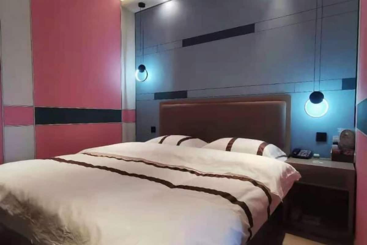 Una habitación de hotel con cama, mesita de noche y lámpara fijada a la pared.