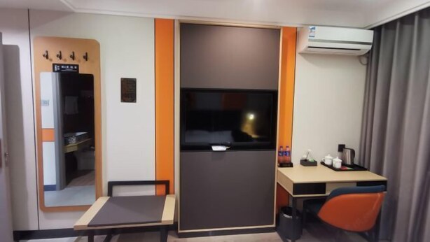 A compact hotel room with a desk, chair, and a small table. There is a wardrobe, a mirror, and an air conditioning unit. - Wanhao Business Hotel (New Barag Right Banner)