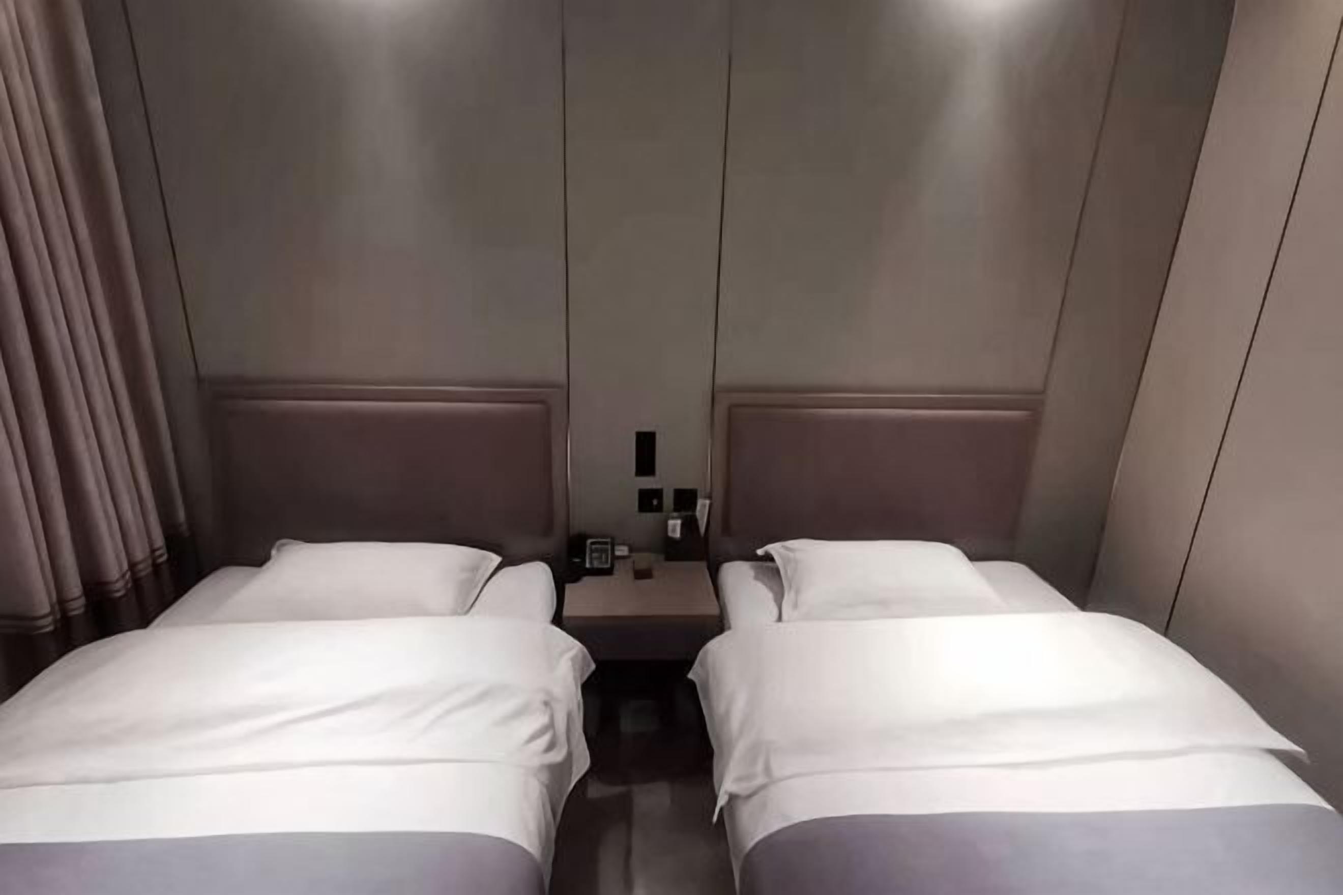 A hotel room with two beds, a nightstand, and a wall-mounted phone.