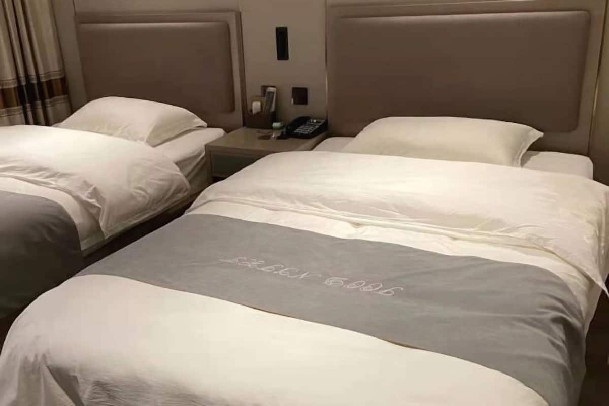 Habitación de hotel con dos camas, una mesita de noche con teléfono e iluminación en la pared.