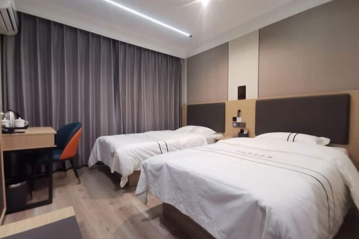 Habitación de hotel con dos camas, un escritorio con silla, una cafetera y una cortina.
