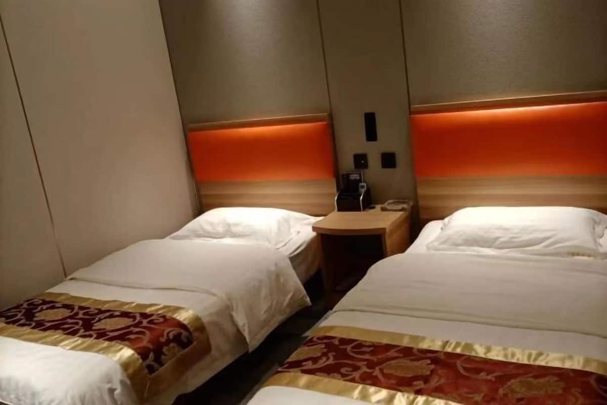 Una habitación de hotel con dos camas, una mesita de noche y una lámpara fijada a la pared.