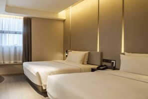 A hotel room with two beds, a large window with curtains, and a bedside table with a lamp.
