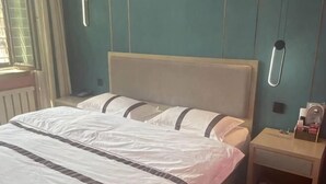 A bed with white bedding and a wooden headboard, a bedside table with a lamp, and a window with curtains. - Wanhao Business Hotel (New Barag Right Banner)