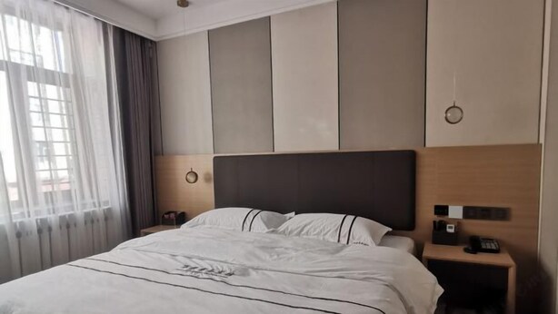 Ein Hotelzimmer mit einem großen Bett, einem Nachttisch mit Telefon und einem Fenster mit Vorhängen.