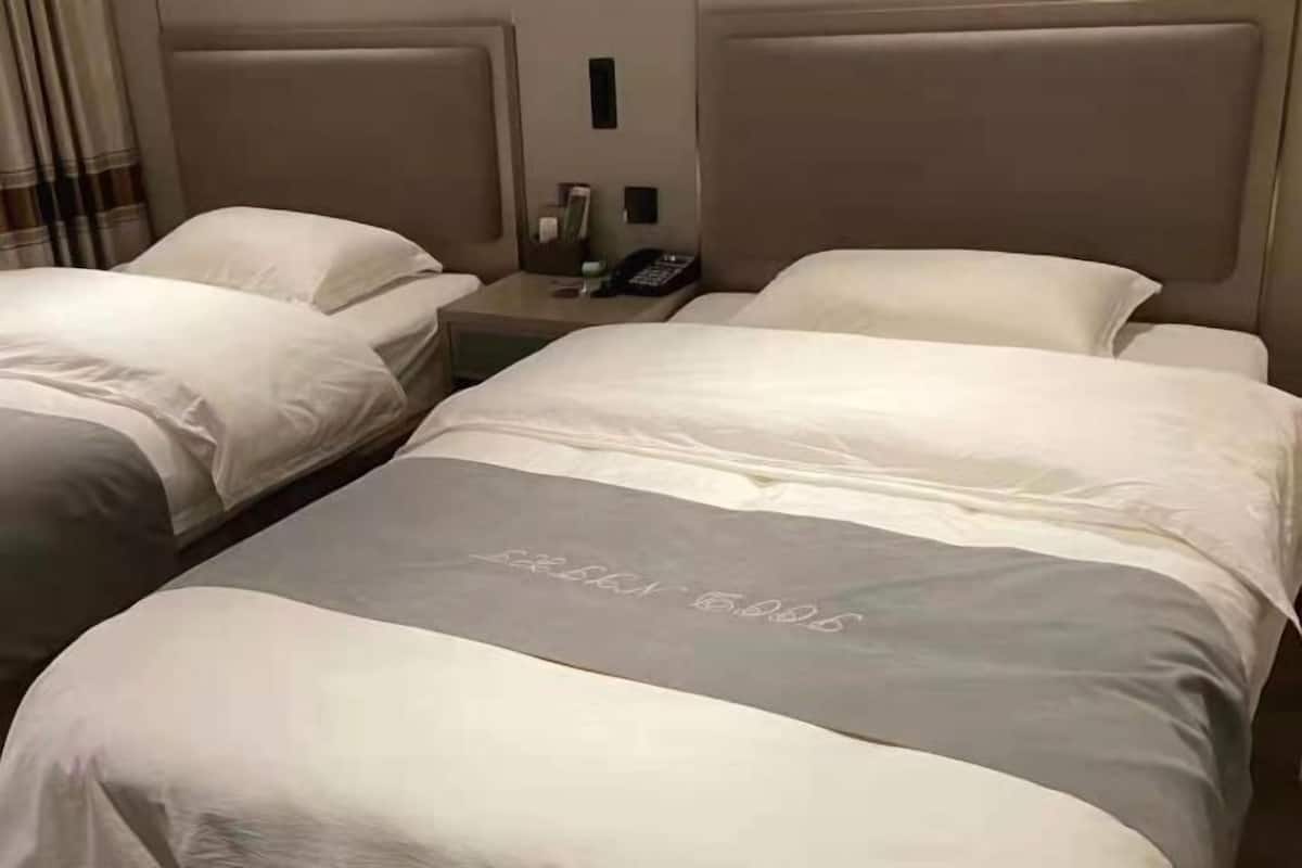 Una habitación de hotel con dos camas, una mesita de noche con un teléfono y una lámpara fijada a la pared.