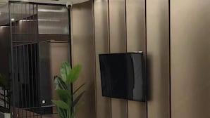 Ein modernes Interieur mit an der Wand montiertem Fernseher, einer Treppe mit Metallgeländer und einer Topfpflanze.