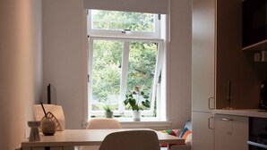 A small, modern kitchen with a white countertop, a chair, and a window with a view of greenery. - Stylish & Modern 2BR Apt, 4min Subway to Oslo City (Oslo)
