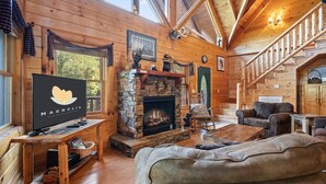 L’intérieur chaleureux d’un chalet en bois, avec une cheminée en pierre, des meubles en bois et un escalier menant à un étage supérieur.