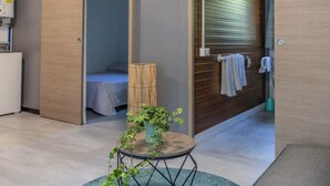 A modern hotel room with a wooden door, a small round table with a plant, a bed with a blue blanket, and a bamboo lamp. - Agricampeggio Princess - (3) (Fiorentina)