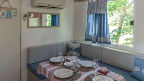 A cozy dining area with a table set for four, a bench with cushions, a window with curtains, and a wall-mounted air conditioner. - Agricampeggio Princess - (3) (Fiorentina)