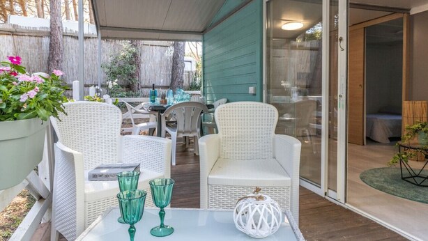 An outdoor patio area with white wicker furniture, a glass door leading to a room, and a table with green glassware. - Agricampeggio Princess - (3) (Fiorentina)