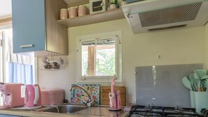 Een keuken met een gasfornuis, een spoelbak en roze apparaten. Er is een raam met uitzicht op groen.