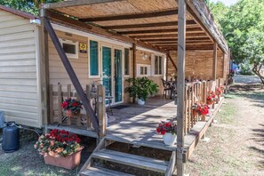 A row of wooden mobile homes with a covered porch, outdoor seating, and potted plants. - Agricampeggio Princess - (5) (Fiorentina)