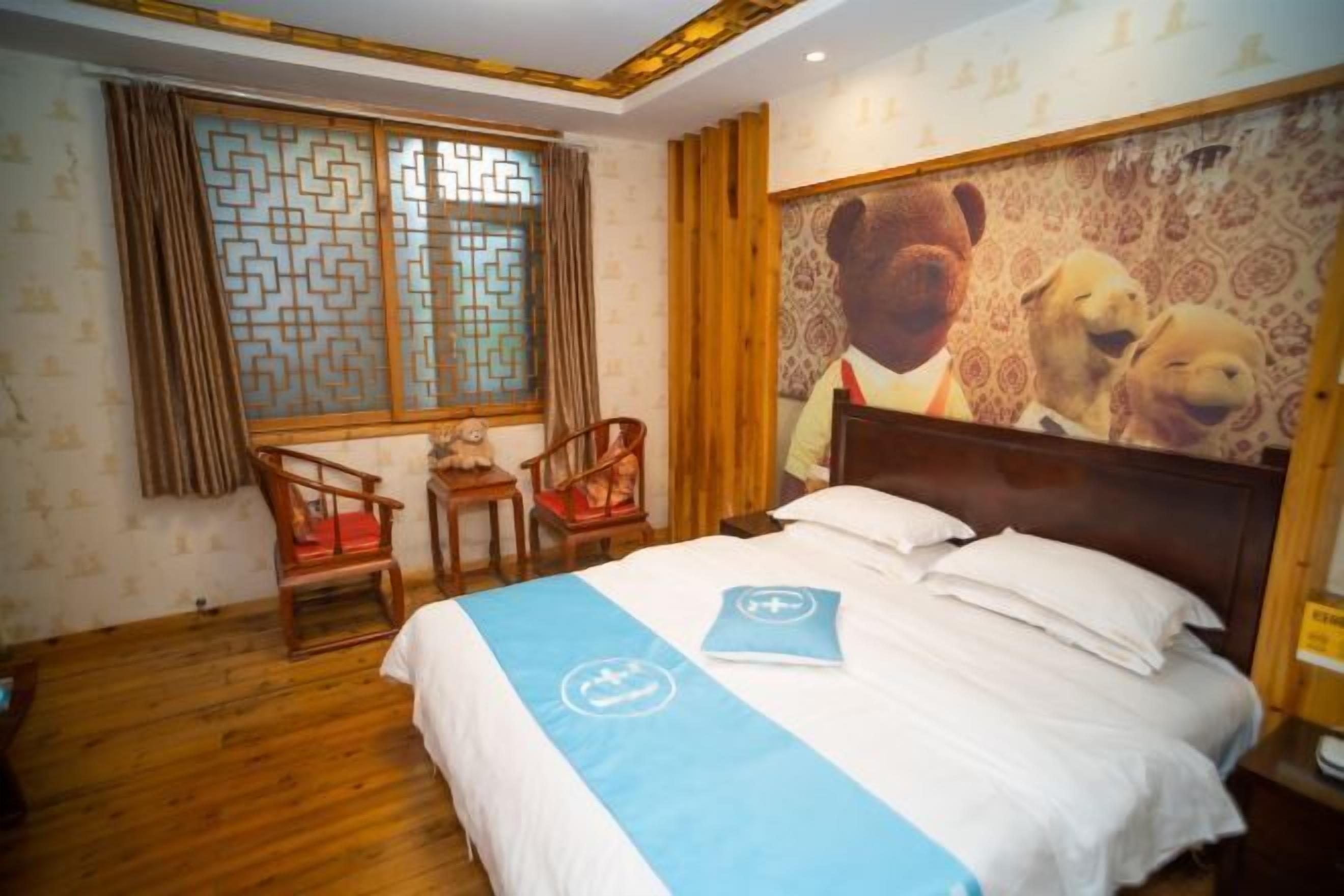Ein Hotelzimmer mit Bett, zwei Stühlen, einem Fenster mit geometrischem Muster und einer Wand mit Wandmalerei von Bär und Hund.
