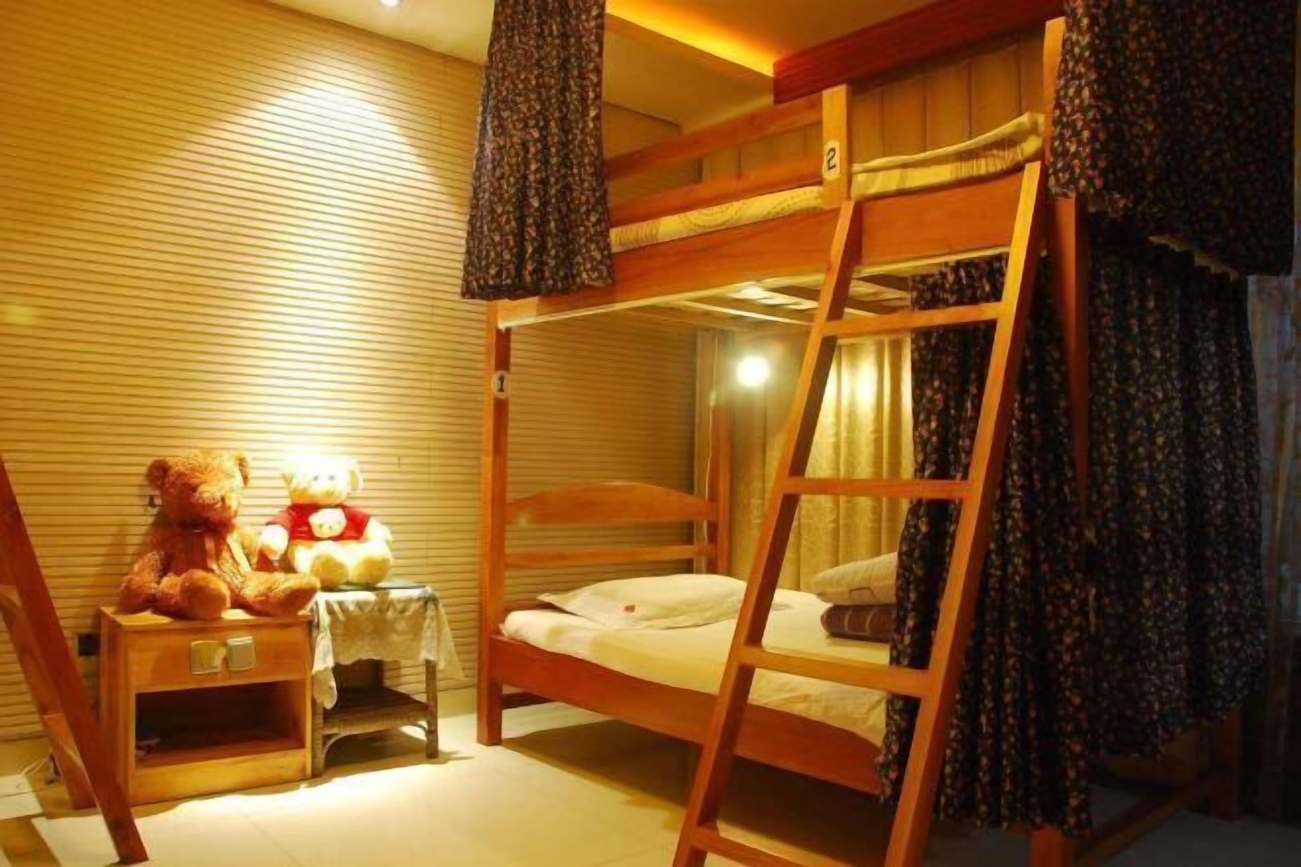 A bunk bed room with a wooden ladder, a small bedside table, and two teddy bears.