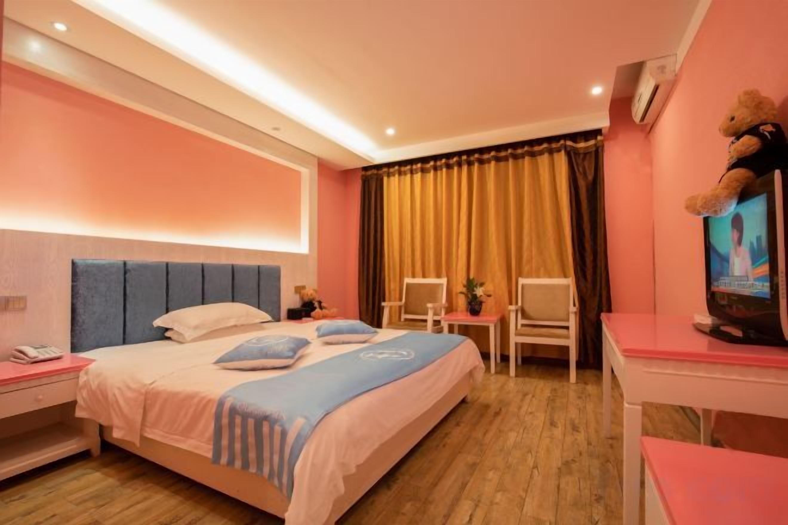 A hotel room with a bed, bedside tables, a desk, a chair, a television, and a teddy bear.