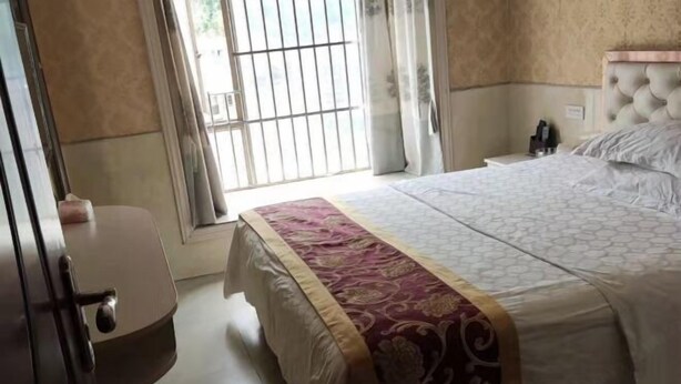 Une chambre d’hôtel avec un lit, une table de chevet, une fenêtre avec des barreaux et une porte.