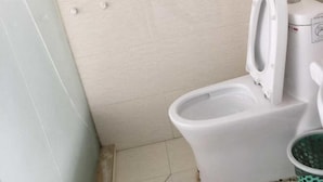 A bathroom with a toilet, a trash bin, and a wall-mounted electrical outlet. - Sinan Yulan Business Hotel (Sinan)