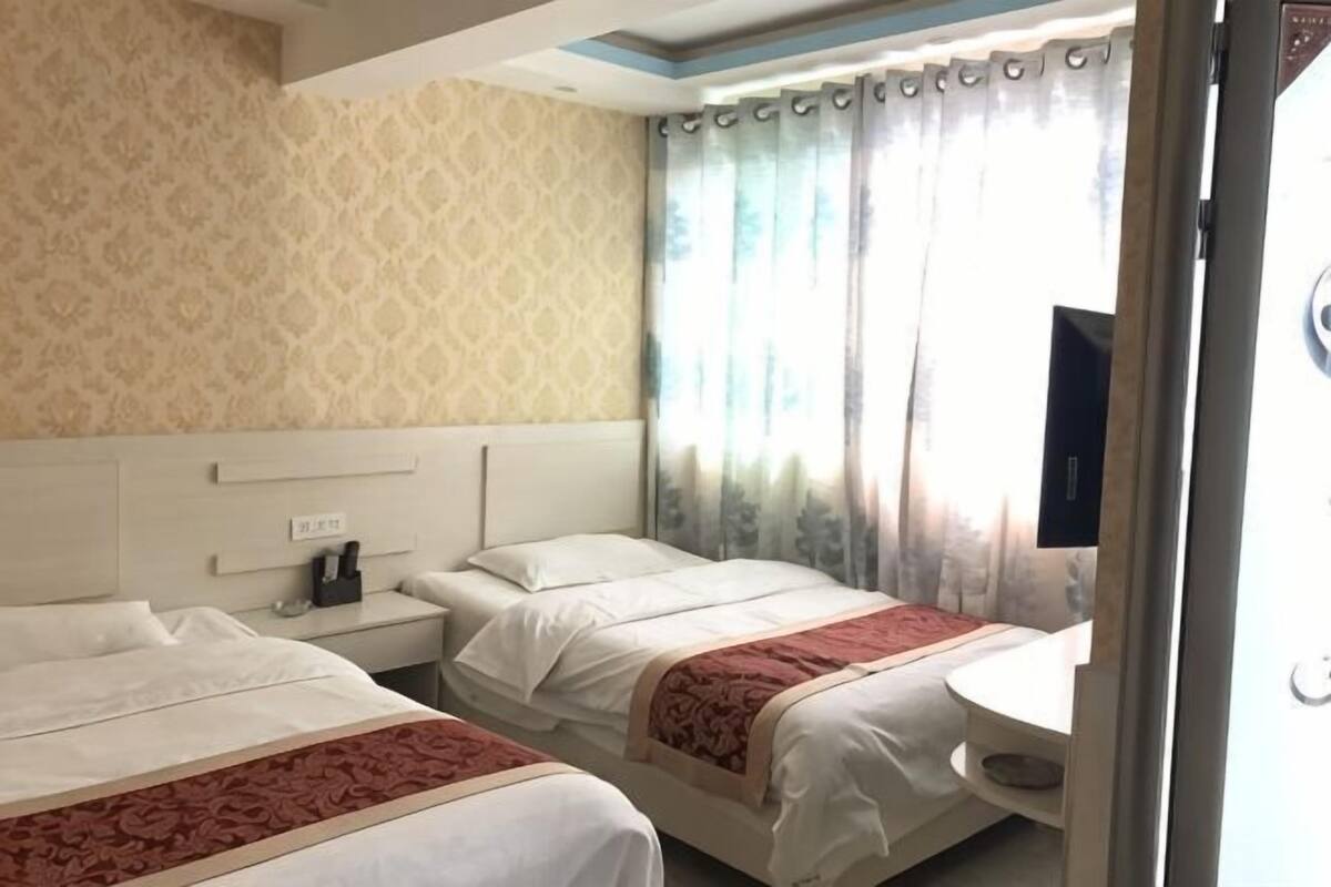 Een hotelkamer met twee bedden, een nachtkastje met lamp, een televisie en een raam met gordijnen.