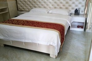 Ein Bett mit weißer und roter Bettdecke, einem gepolsterten Kopfteil und einem Nachttisch mit Flasche und Gläsern.