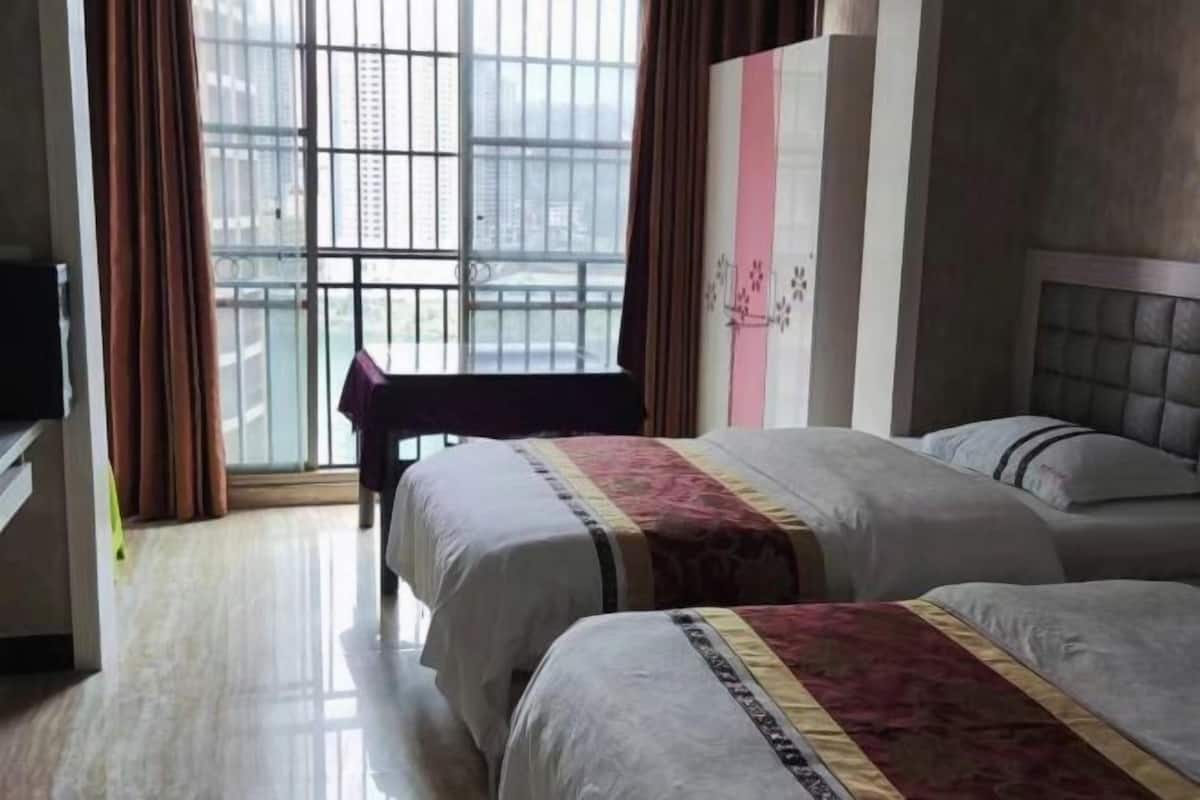 Hotelkamer met twee bedden, een raam met uitzicht op gebouwen, een stoel en een bed met een decoratieve spreidekker.