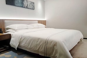 Cama bem arrumada com lençóis brancos e cabeceira de madeira, mesa de cabeceira com abajur e obra de arte na parede acima da cama.