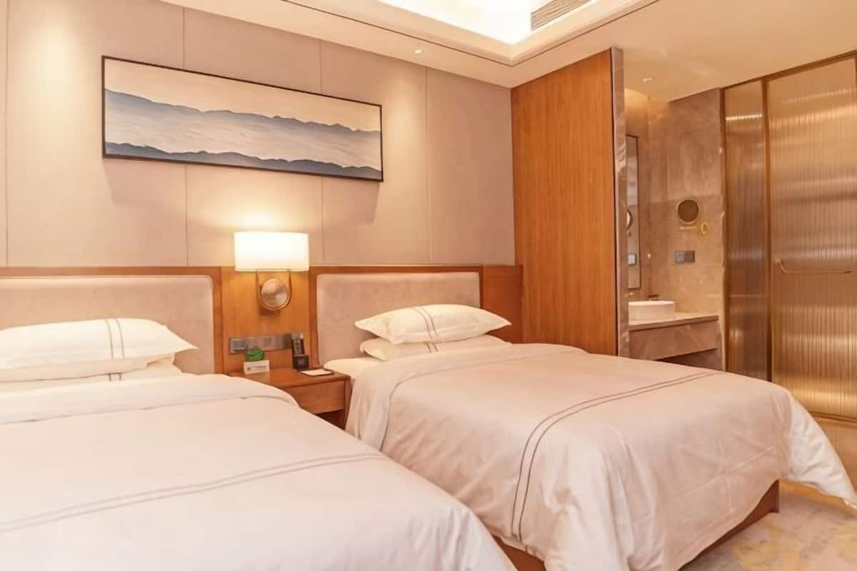 Une chambre d’hôtel avec deux lits, une table de chevet avec une lampe, une salle de bain avec un miroir et une grande fenêtre.