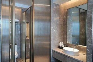 Ein modernes Badezimmer mit Duschkabine aus Glas, einer Marmorfliesenwand und einem großen Spiegel über einem Waschbecken.