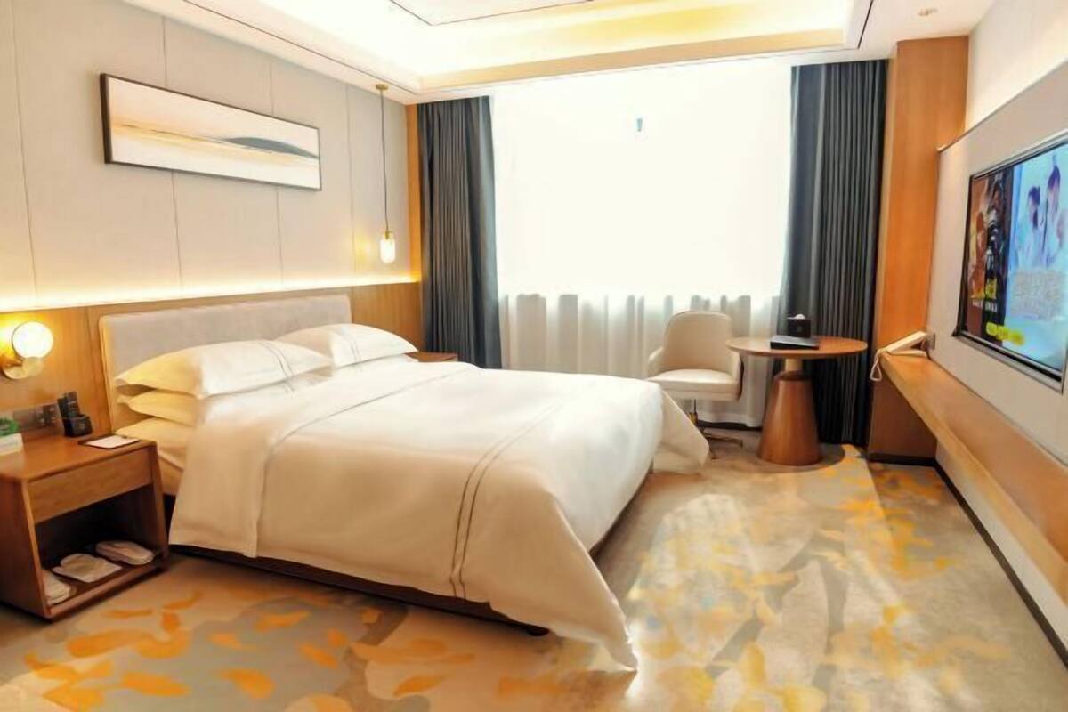 Une chambre d’hôtel avec un lit, une table de chevet, une lampe et un téléviseur fixé au mur.