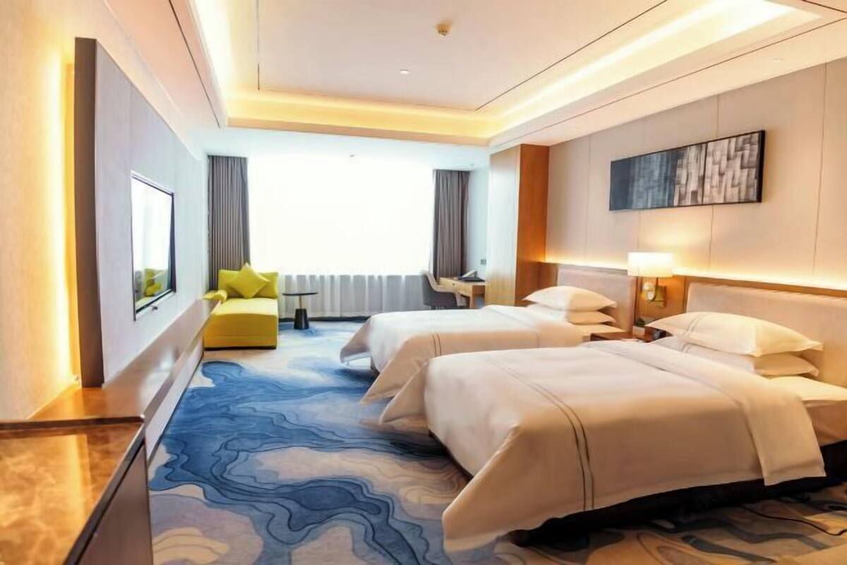 Une chambre d’hôtel avec deux lits, un canapé, un bureau et une grande fenêtre.