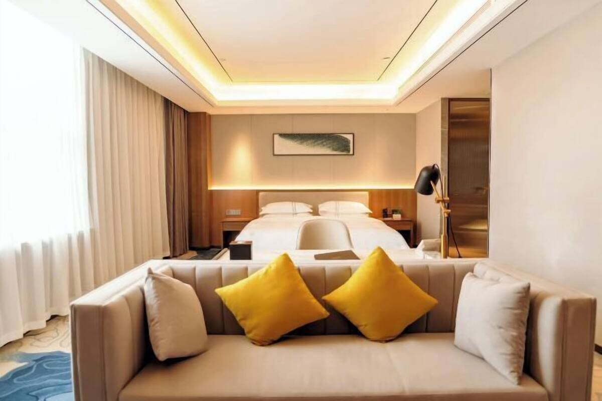 Une chambre d’hôtel avec un lit, un canapé avec des coussins, un bureau, une lampe et un tableau au mur.