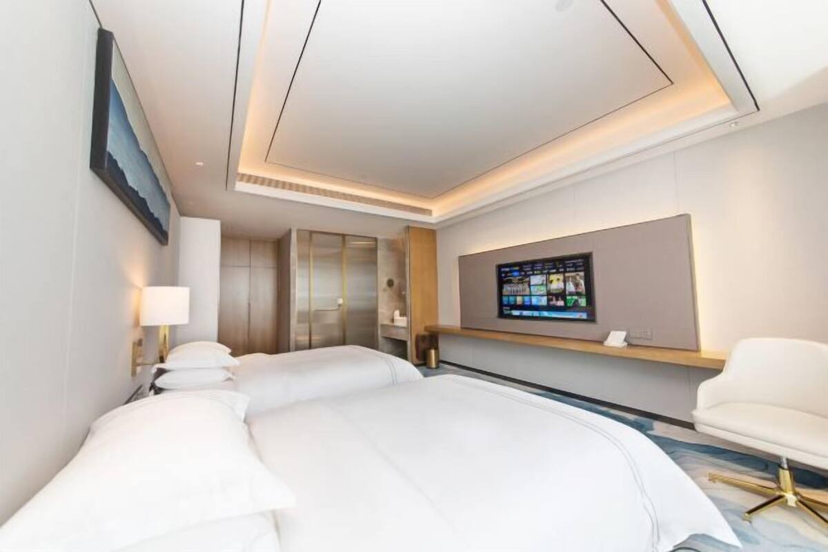 Une chambre d’hôtel moderne dotée d’un grand lit, d’un téléviseur fixé au mur et d’un coin salon avec un fauteuil.