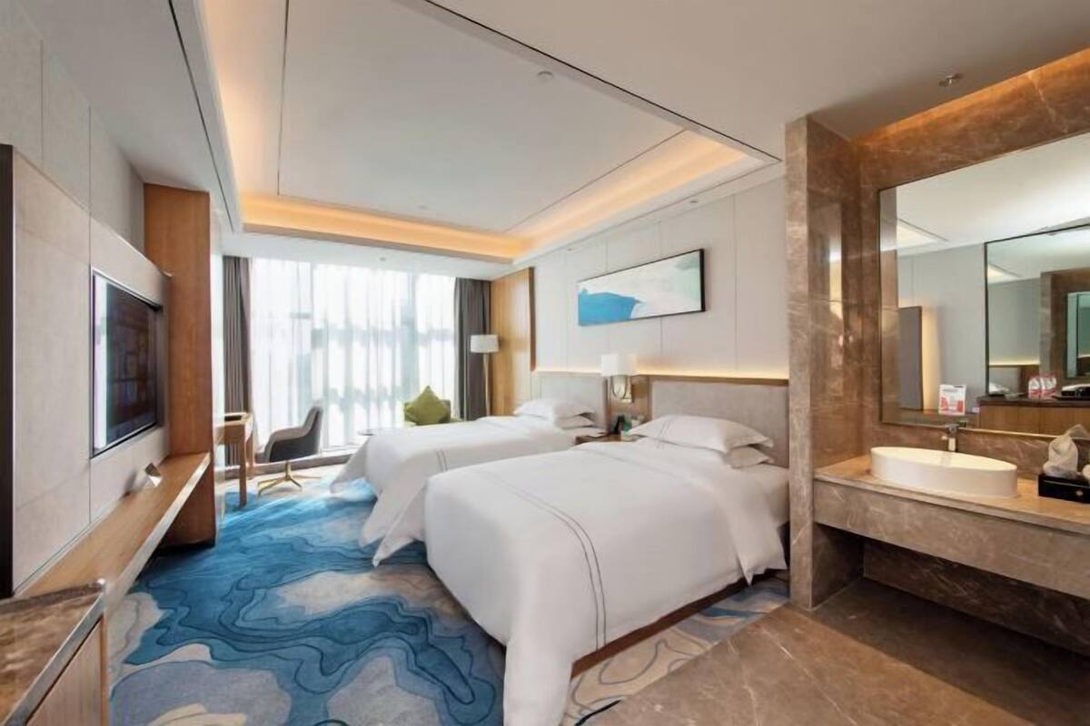 Une chambre d’hôtel avec deux lits, un grand miroir, une télévision et une salle de bain dotée d’un comptoir en marbre.