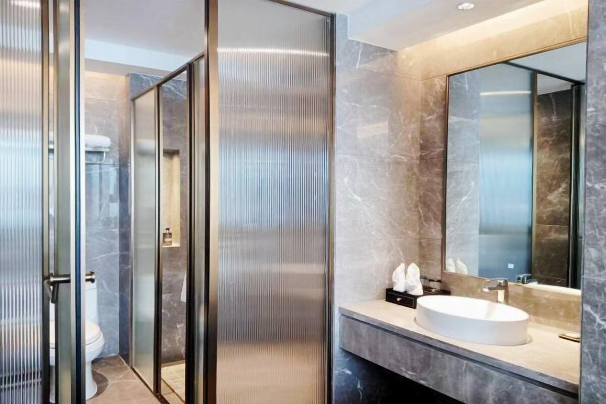 Une salle de bain moderne avec une douche à parois de verre, un lavabo en marbre et un grand miroir.