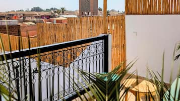 A wooden pergola with hanging baskets, a metal railing, and a view of a cityscape with a tall tower.