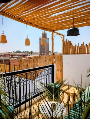 Una pèrgola de fusta amb cistells penjants, una barana metàl·lica i una vista d'un paisatge urbà amb una torre alta.