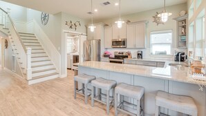 A spacious kitchen with a large island, bar stools, stainless steel appliances, and a staircase leading to another level. - Walk to Sea Isle Beach! Canal-front Gem w/ Pool (Galveston)