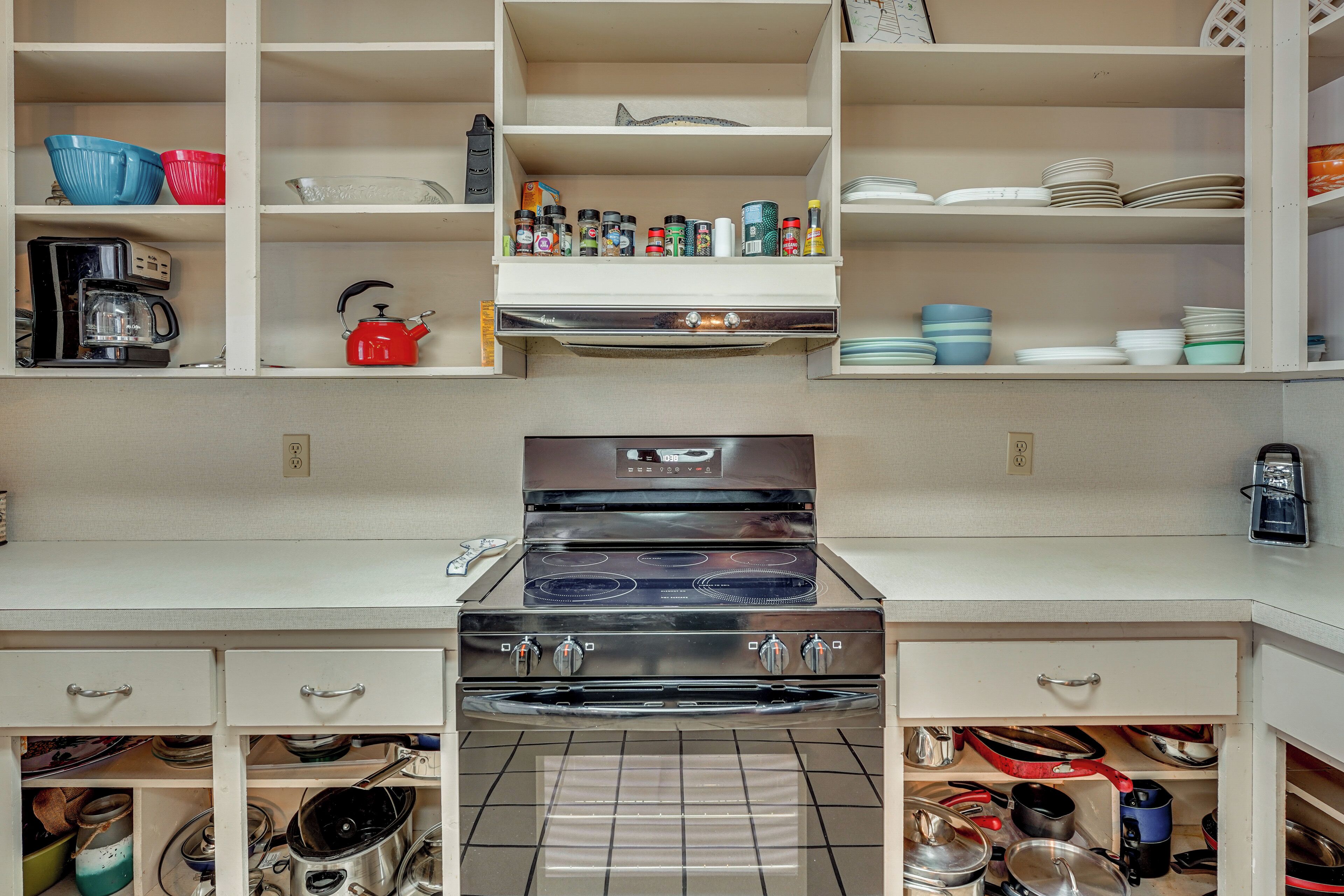 A kitchen with a stove, oven, and various kitchen items on shelves.