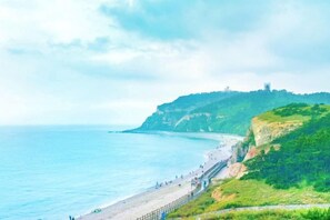 A coastal landscape with a beach, cliffs, and a distant structure. - Zanzan Hotel (Yantai)