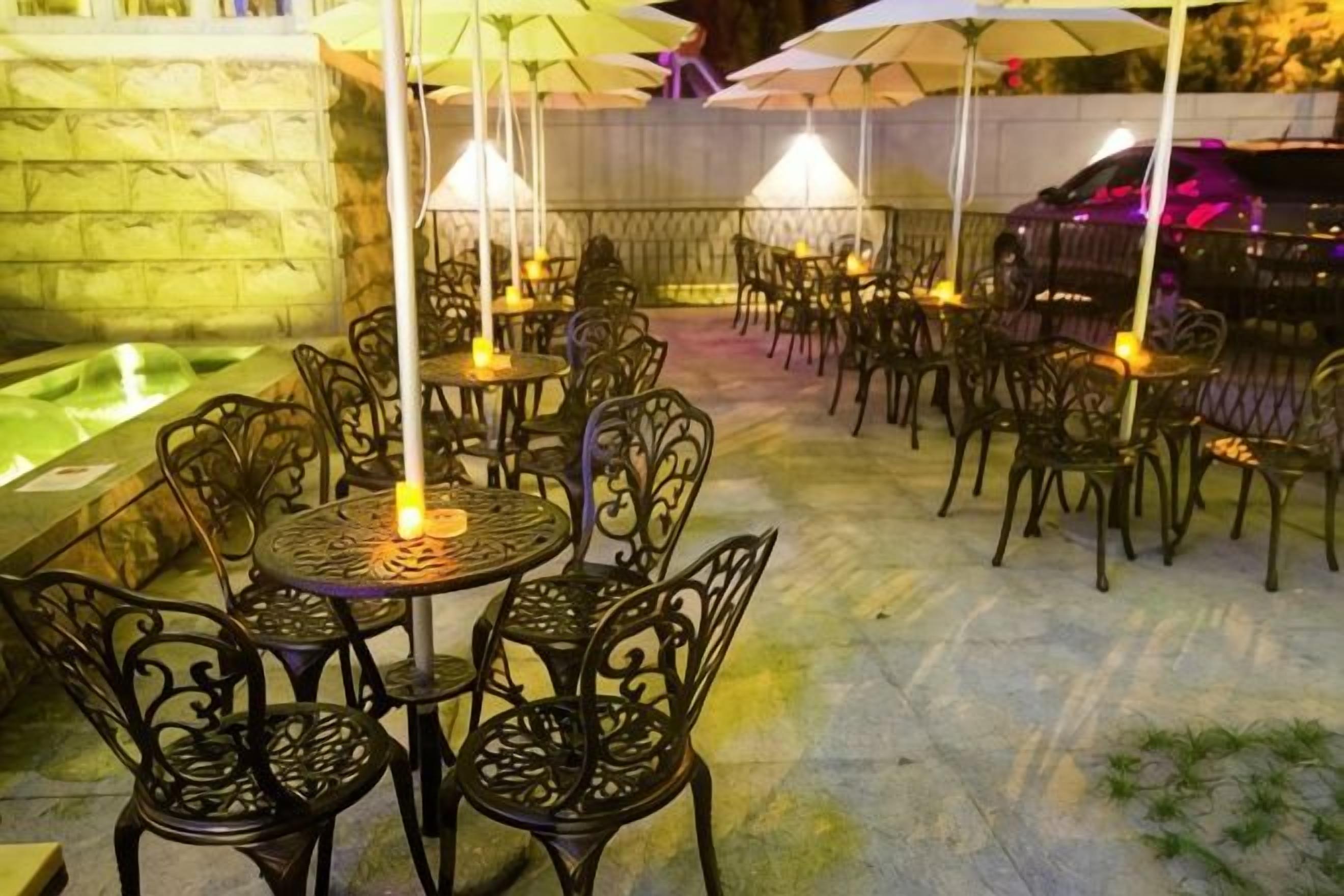 An outdoor patio with round tables and chairs, umbrellas, and a stone wall.