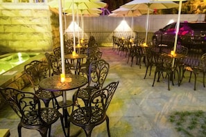 Une terrasse extérieure avec des tables et des chaises rondes, des parasols et un mur en pierre.