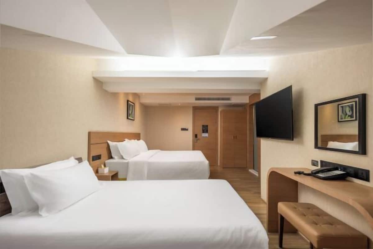 A hotel room with two beds, a desk, a TV, and a mirror.