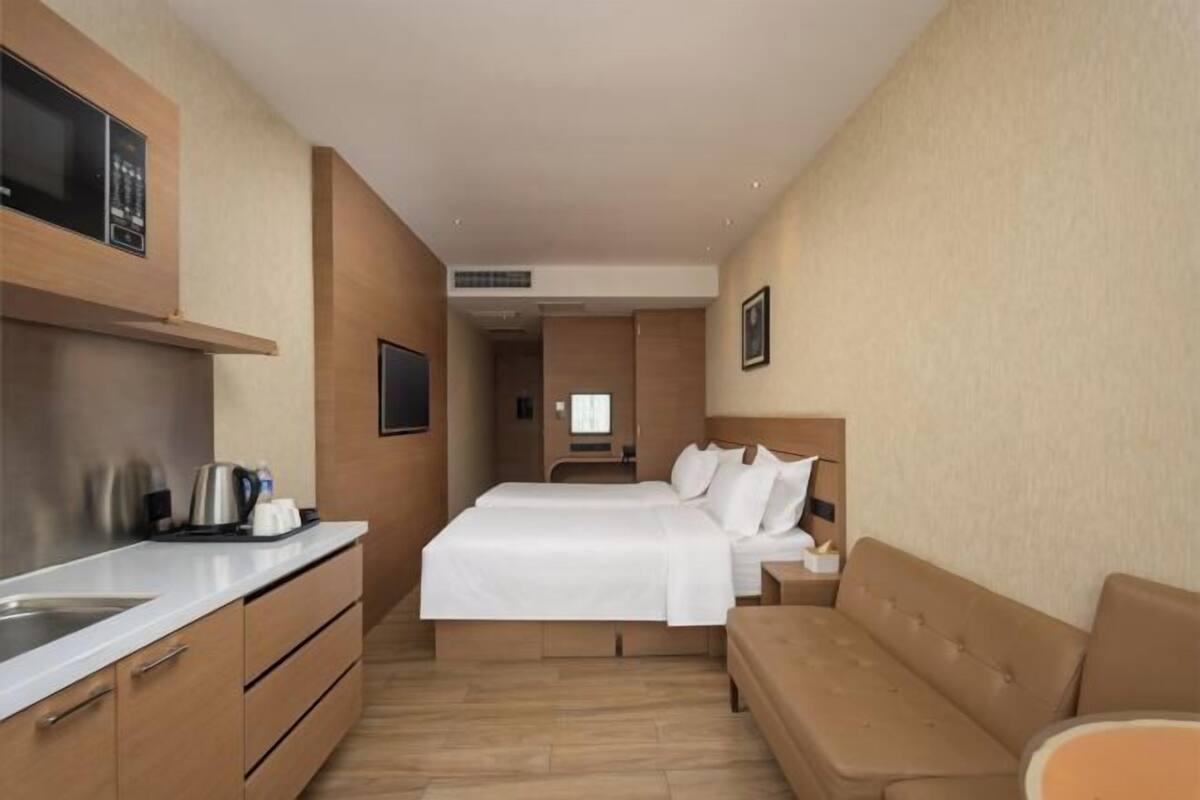 A hotel room with a bed, a sofa, a desk with a kettle, and a TV.