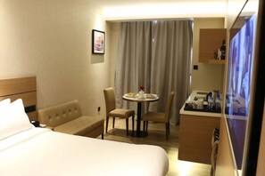 A hotel room with a bed, a seating area with a table, a TV, and a kitchenette. - Zanzan Hotel (Yantai)