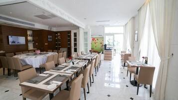 Un comedor de hotel con varias mesas y sillas, un televisor y una estantería para vinos.